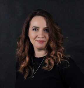 Smiling woman with curly hair on black background.